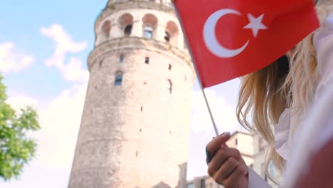 slow motion:attractive young beautiful girl waves turkish flag in front of galata tower,a popular landmark in istanbul,turkey