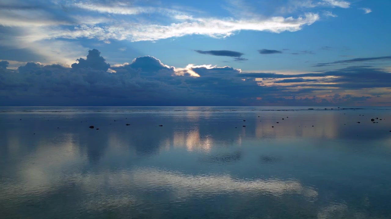 Calm ocean water reflecting a dramatic cloudy sky during a peaceful sunset creating a serene atmospheric landscape. Magic aerial view overflight flyover drone panorama