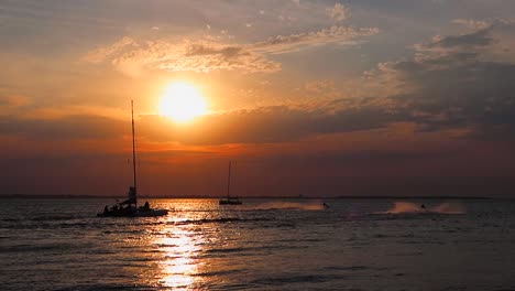 velero y motos de agua en aguas del mar al atardecer