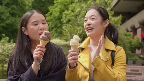 Two-Smiling-Young-Female-Friends-Meeting-And-Eating-Ice-Cream-Outdoors-In-Park-Together-4