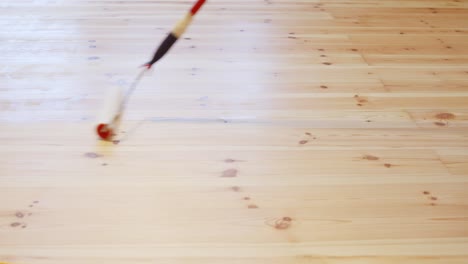 detailed view of a paint roller coating a pinewood floor with clear primer during home renovation, wood texture and product sheen visible on surface, static shot