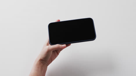 Video of caucasian woman&#039;s hand holding smartphone with blank screen on white background