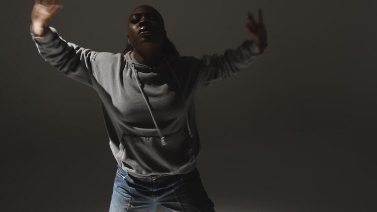 Studio Portrait Shot Of Young Woman Wearing Hoodie Dancing With Low Key Lighting Against Grey Background 10