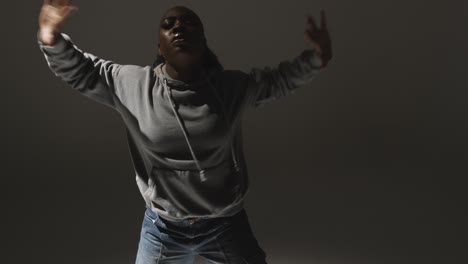 Studio-Portrait-Shot-Of-Young-Woman-Wearing-Hoodie-Dancing-With-Low-Key-Lighting-Against-Grey-Background-10