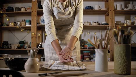 young woman potter puts the clay on the table and using a rolling pin to flatten it