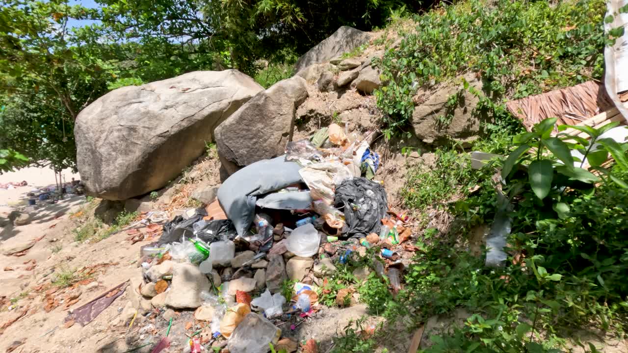 Daytime camera pans from trash pile to beach, highlighting environmental pollution and natural surroundings