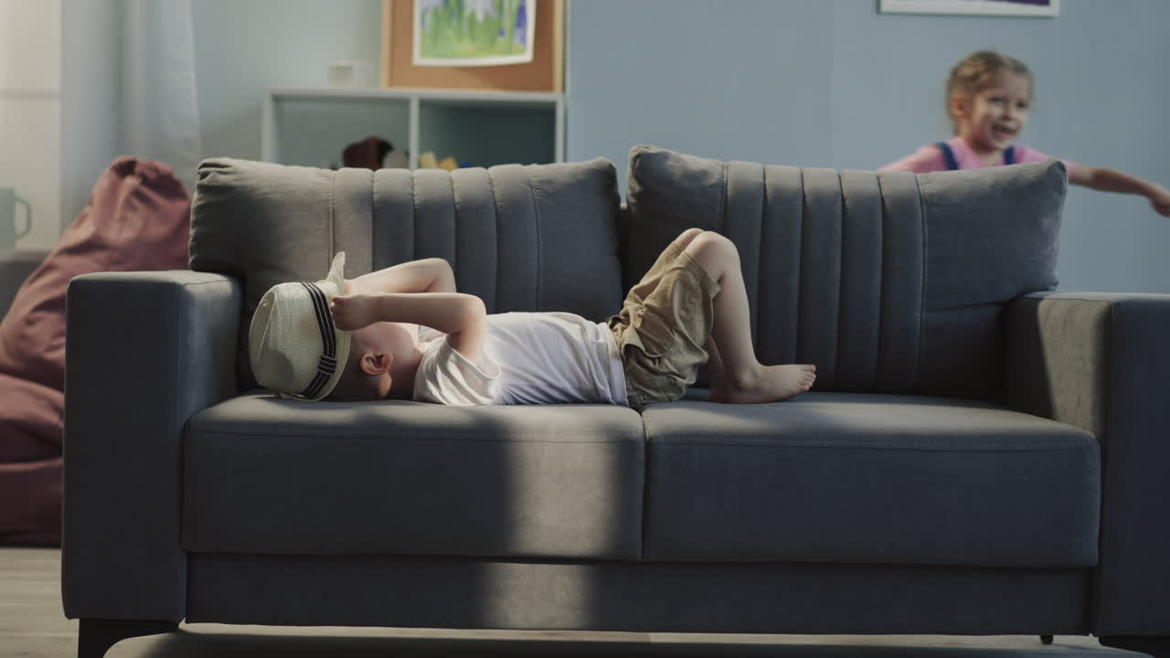 소녀는 소파 주변에 가방을 끌고 동생은 파나마와 놀고 있습니다.