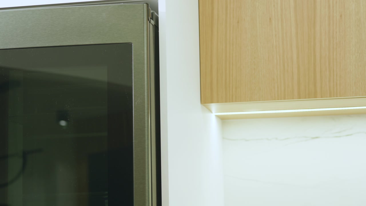 Close-up shot showing the edge of a stainless steel appliance next to a light wood cabinet with a warm light strip embedded in its base