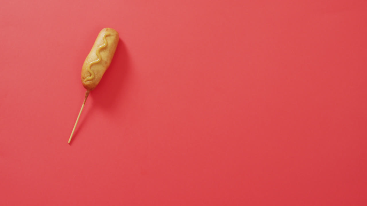 video de un perro de maíz con mostaza en una superficie roja