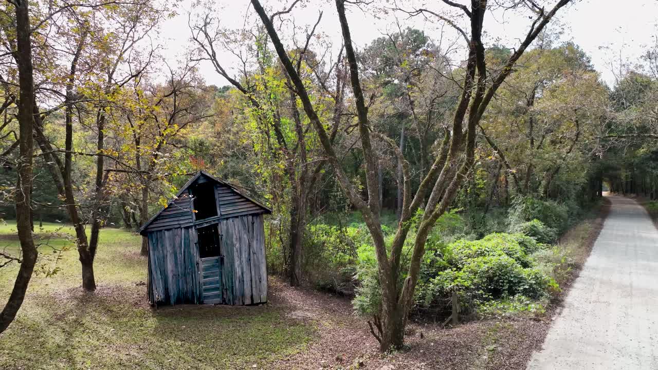 오른쪽 비포장 도로 옆 숲에 손상된 오래된 창고와 창백한 하늘