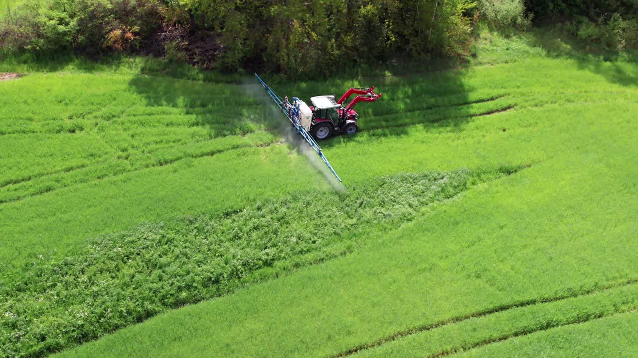 Un agricoltore guida un trattore attraverso un campo verde irrorando erbicida.