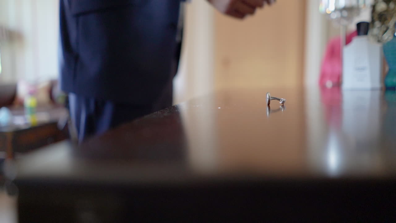 Picking up cuff links from the table by a man front of the dressing table