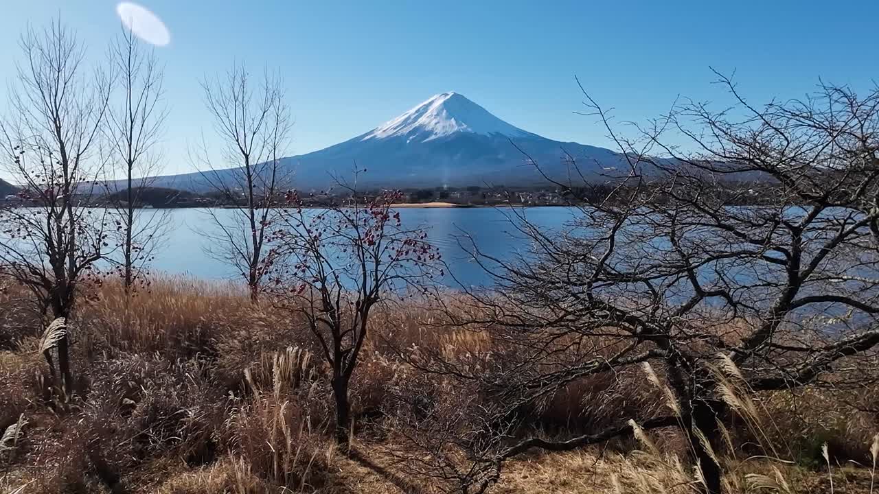 Udsigt over Fuji-bjerget fra flodbredden med en spejling af bjerget i floden og sne på toppen af bjerget.