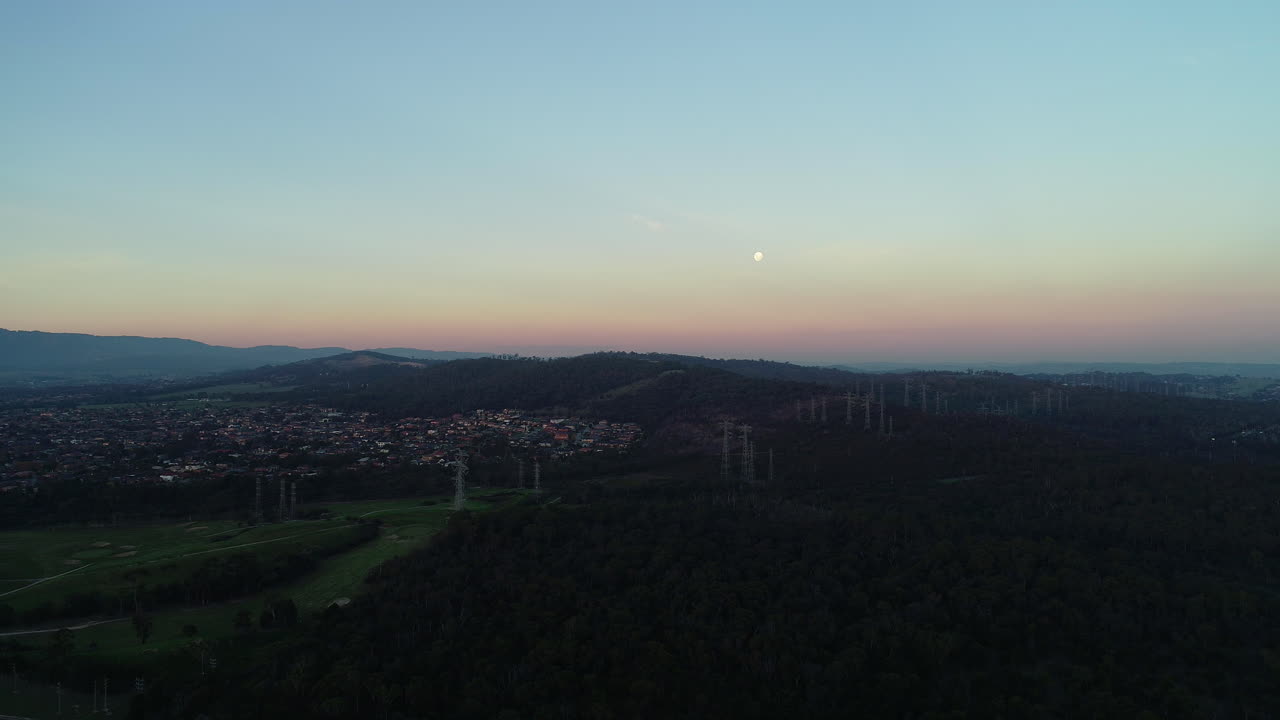 Smooth vertical aerial accent over dark landscape with power lines strung together.