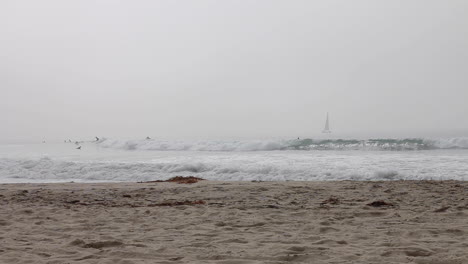 Capa-Marina-Sobre-La-Playa-De-Venice,-Ca-Mientras-Los-Caminantes-Pasean-Y-Los-Surfistas-Golpean-Las-Olas