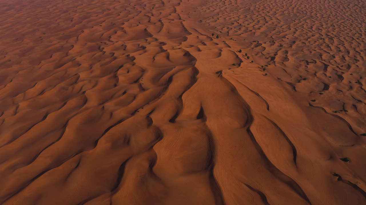 Vista a volo d'uccello di veicoli che attraversano vaste dune di sabbia dorata al tramonto nel deserto.