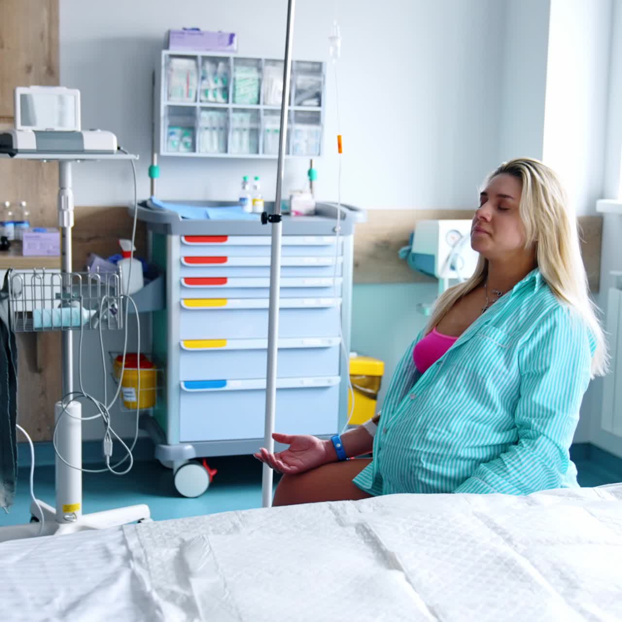 Pregnant woman sits on a fitball in the hospital ward. Modern medical equipment at backdrop