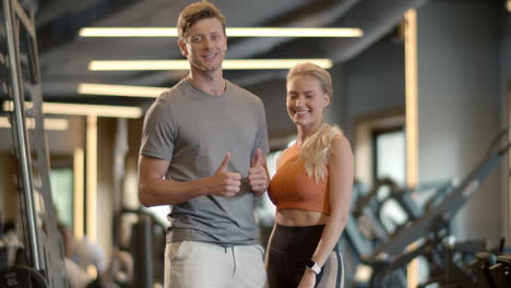 Cheerful-couple-enjoying-results-in-sport-club.-Fit-man-showing-like-sign-at-gym