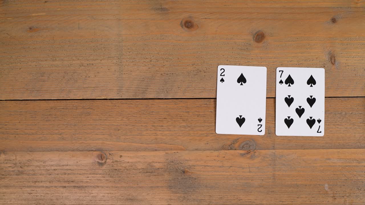 A person laying out a Deuce on a wooden table to educate the viewer on how to play poker