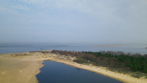 Toma-Lateral-Aérea-Del-Lago-Mikoszewskie-Y-El-Río-Vistula-Terminó-En-El-Banco-De-Arena-De-La-Reserva-Natural-Mewia-Lacha-Durante-Un-Día-Soleado,-Mar-Báltico-En-Segundo-Plano