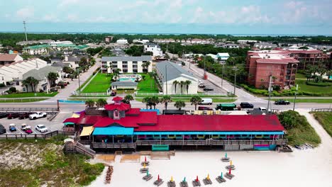 pompano joe's restaurant and parking lot trucking right aerial drone shot with a view of old 98, white sand, emerald green water and lots of umbrellas and beach chairs in destin florida