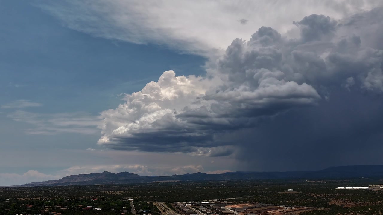 Timelapse 4K UHD realizzato con drone che cattura l'imponente fronte d'avanzamento di un'intensa tempesta monsonica. Un muro denso e scuro di nuvole di pioggia intense contrasta nettamente con il cielo azzurro rimanente sopra la valle.