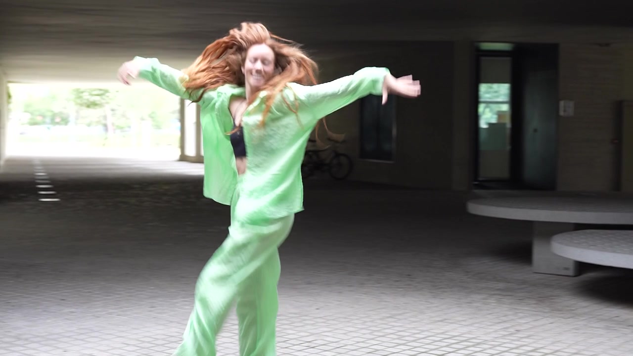 近代的な建物の通路の下で、鮮やかな緑色の服装で踊る幸せそうな女性。