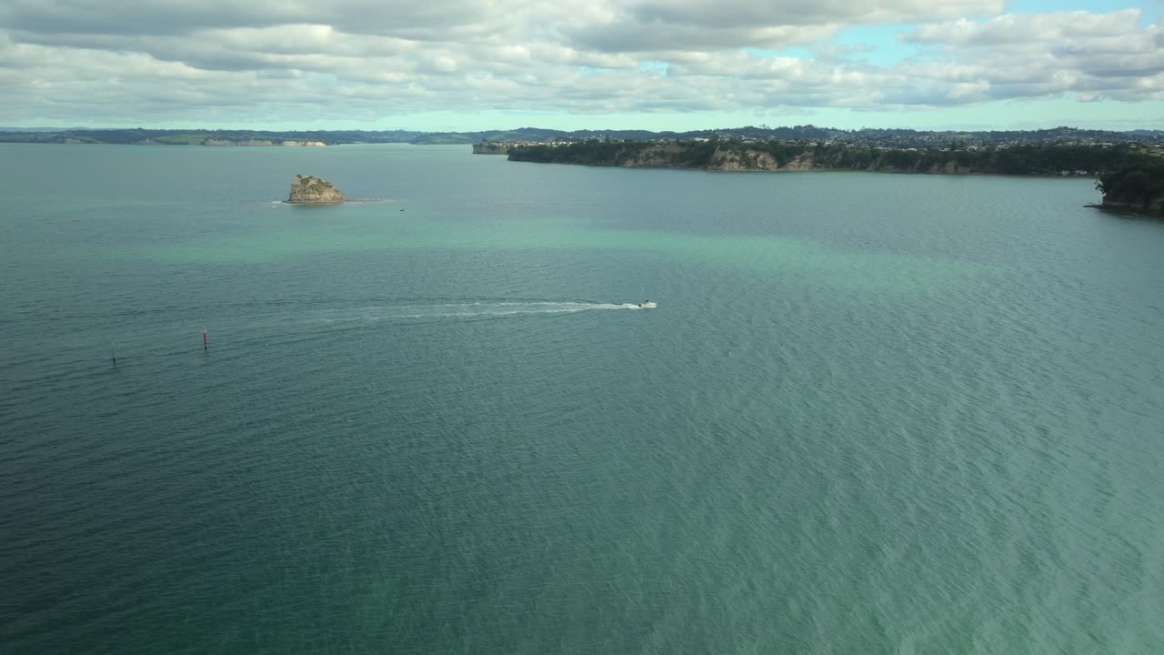 Ripresa aerea di un motoscafo che naviga vicino a scogliere rocciose e una grande formazione rocciosa nell'oceano sotto un cielo sereno