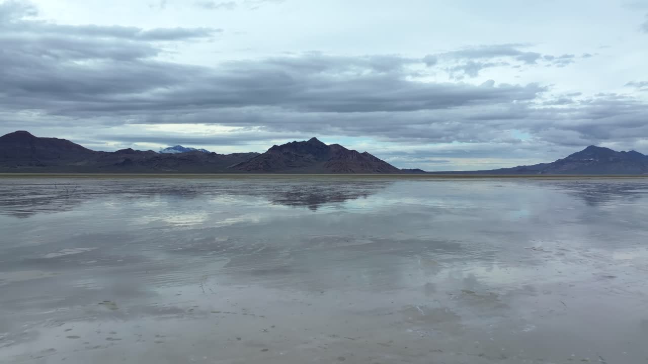 Wide Aerial drone dolly out shot of the famous Bonneville Salt Flats in Utah near Wendover, Nevada flooded from rain, creating mirage reflections with mountains on a stormy spring evening
