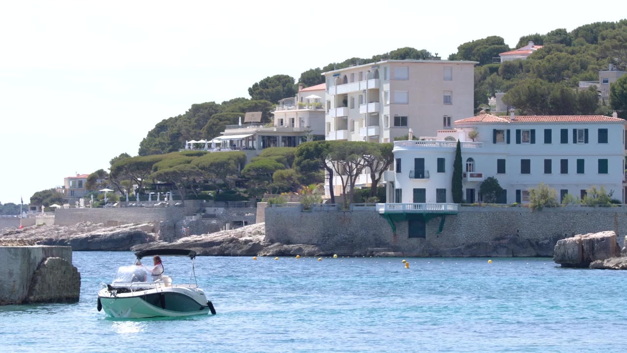 Una piccola barca a motore naviga su acque blu vicino a coste rocciose e appartamenti sulla costa a Cassis.