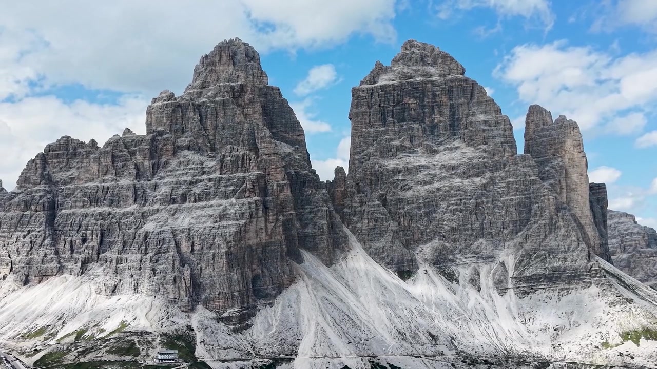 Vista ravvicinata cinematografica da drone delle iconiche Tre Cime di Lavaredo che si ergono sul paesaggio alpino nelle Dolomiti, Italia.