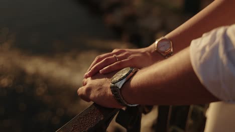 close up of couple’s hands with wristwatches and engagement ring at sunset moment
