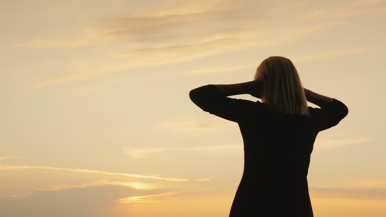 silueta de una mujer mirando al cielo después de la puesta de sol vista trasera