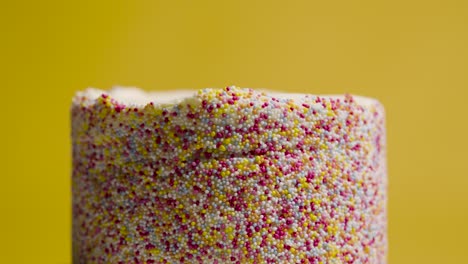 close up studio shot of revolving birthday cake covered with hundreds and thousands decorations 7