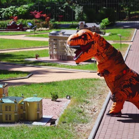 big dragon in the park. person in dragon costume walking among small city with handmade buildings outdoors.