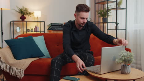 young guy freelancer starts working on laptop, sends messages, makes online purchases at home