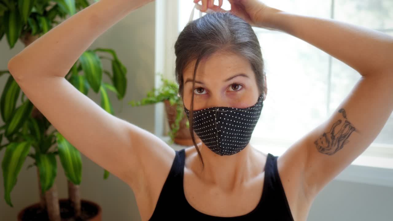 Attractive young woman wearing medical mask attempting to untie it but fails and gets stuck