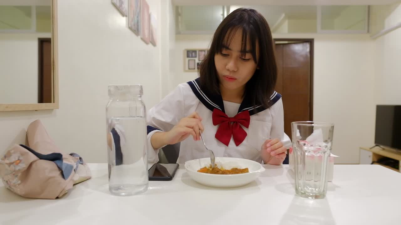 Woman happily claps hands at dining table and eats rice dish with spoon