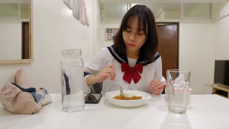 woman happily claps hands at dining table and eats rice dish with spoon