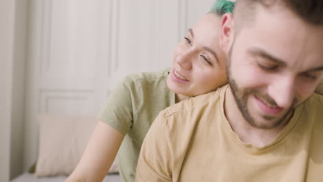 young woman resting her head on her boyfriend's shoulder while sitting together on the bed