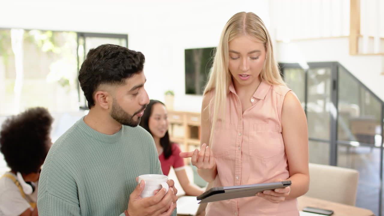 Discussing project, young diverse friends using tablet and holding coffee cup indoors