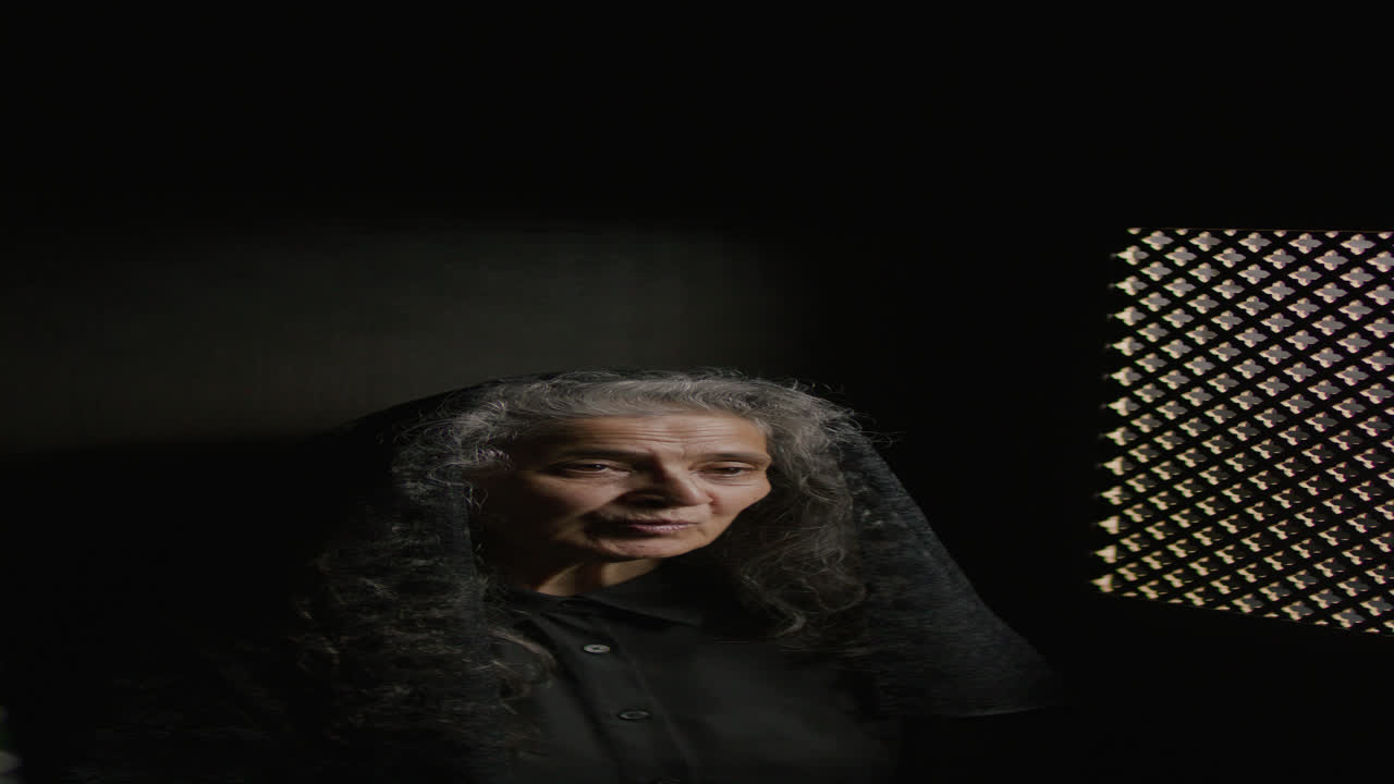 Elderly Female Parishioner in Black Veil Speaking in Confessional Booth
