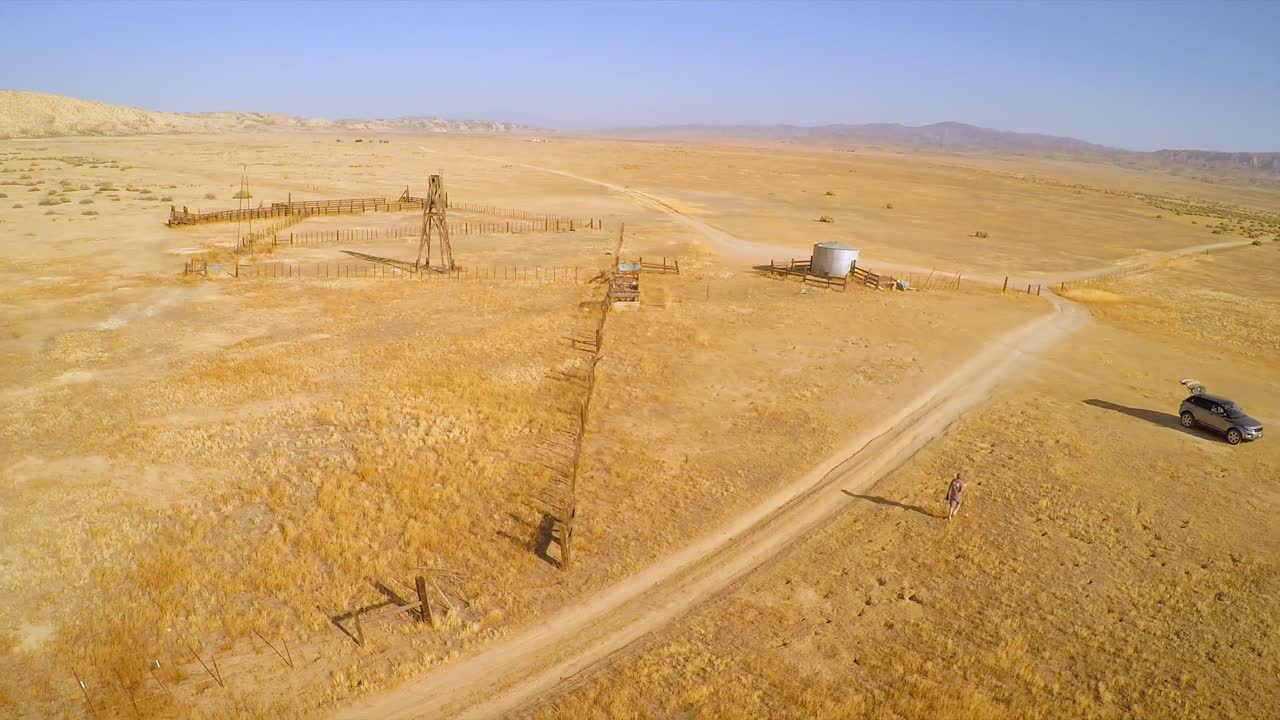 una antena sobre un hombre que camina hacia su auto cerca de un rancho abandonado en el desierto de la llanura del carrizo