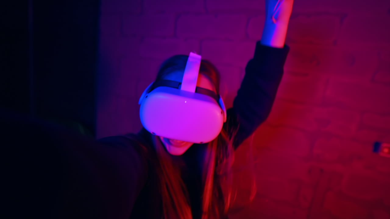 A young interested woman playing in VR games using VR glasses and controllers, filming herself on camera. Red and blue illumination. Slow motion