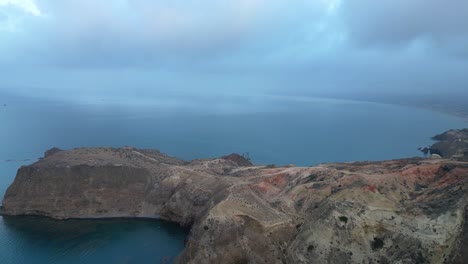 Soaring-gracefully-above-a-rugged-cliff,-seizing-a-mesmerizing-top-down-view-of-the-tranquil-Mediterranean-Sea-on-a-cloudy-day