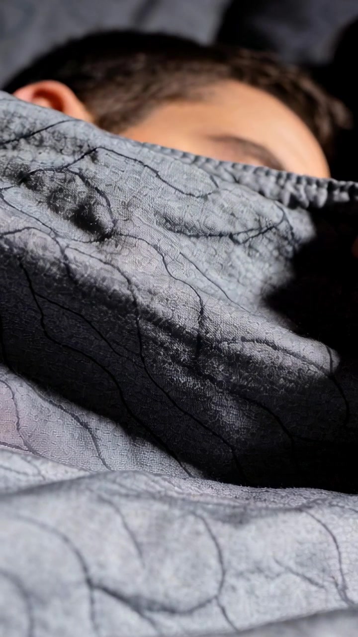 Video verticale: Una mano che si allunga, un uomo adulto che tira su un piumino trapuntato grigio sul letto, in cerca di calore