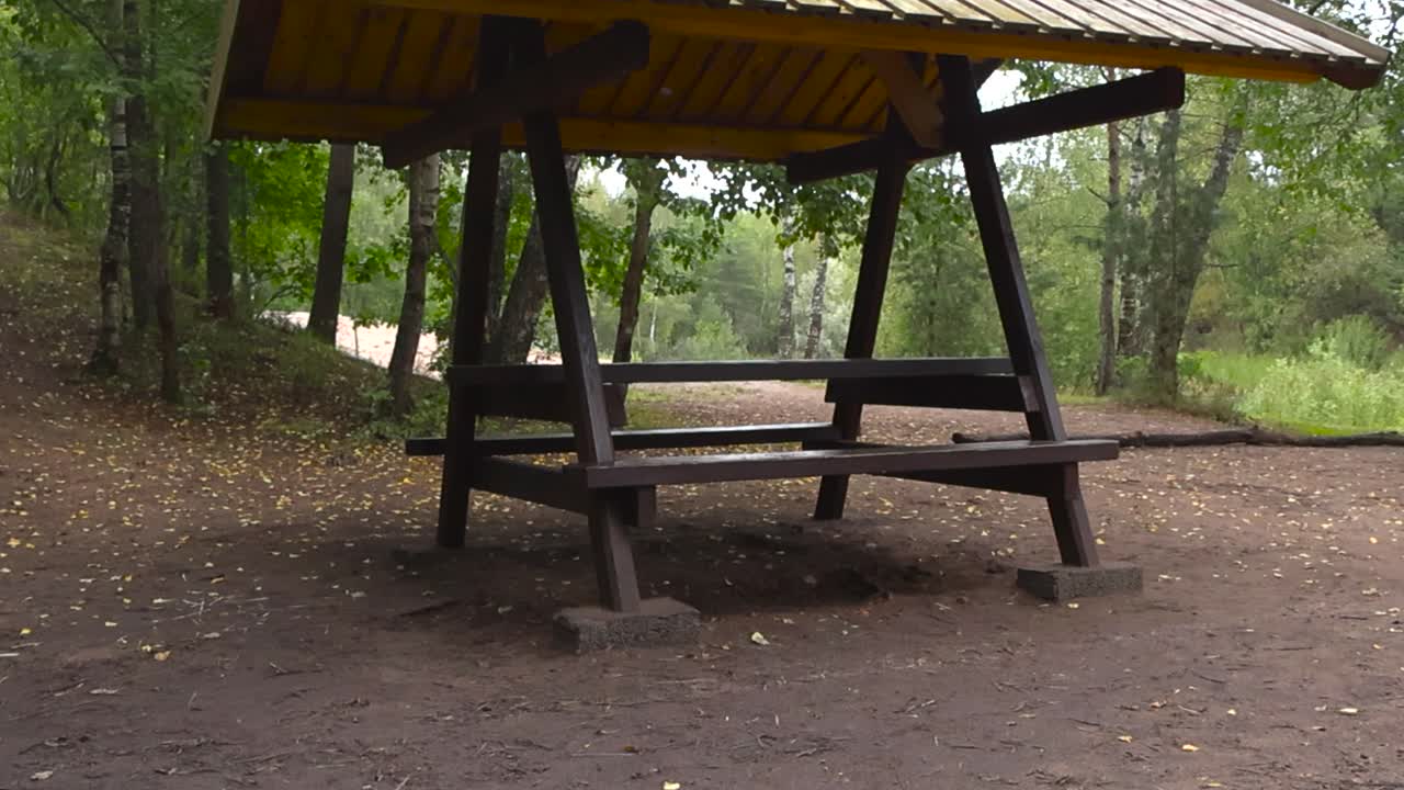 Afslørende video af et gult afspærringsbånd, der hænger foran en campingplads eller et grillsted i en landlig skov om sommeren. Ingen personer er synlige. Video med skiftende fokus