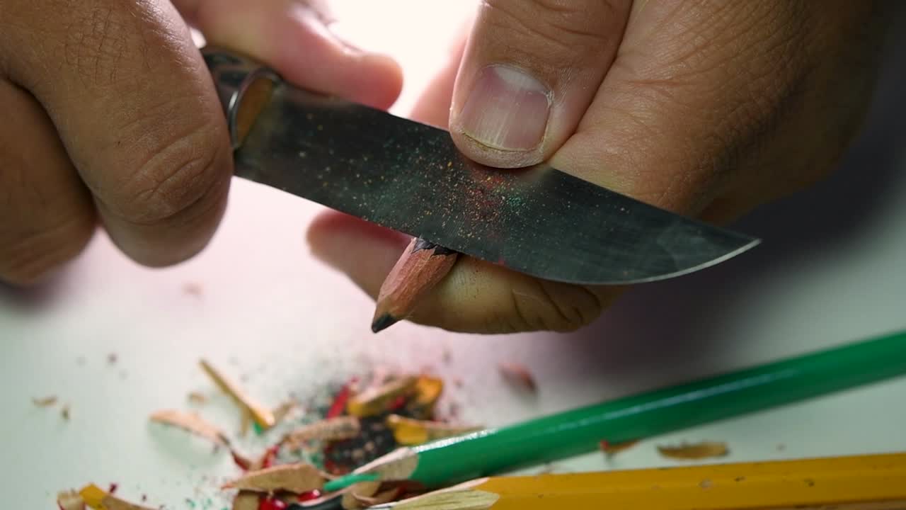 Opptak av hender som sakte spisser en blyant og noen fargeblyanter med en skarp kniv