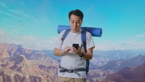 Asian Male Hiker With Mountaineering Backpack Looking At The Smartphone And Saying Wow While Traveling At The Top Of Mountain