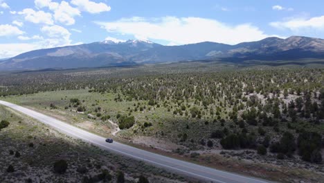 drone shot of car driving down the highway, panning up to reveal the vast, forested valley and wheeler peak rising from the valley floor. high desert landscape with tall mountains and blue sky.